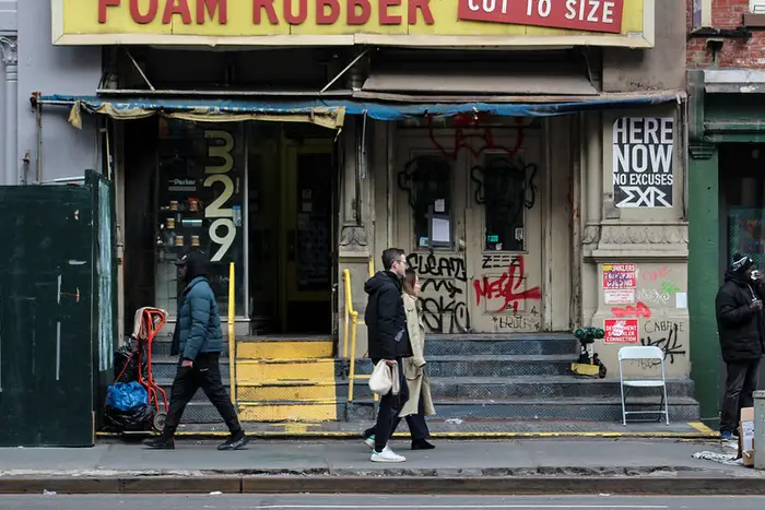 a few people walk down Canal Street in front of a foam rubber shop